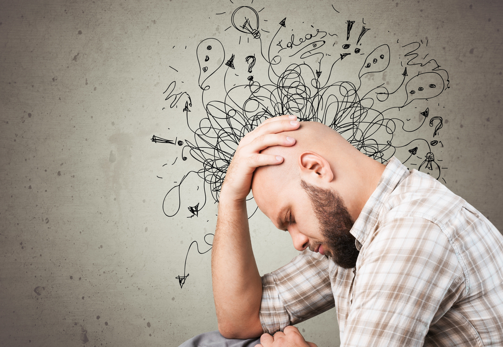 Bald man in light plaid shirt looking stressed with hand on head