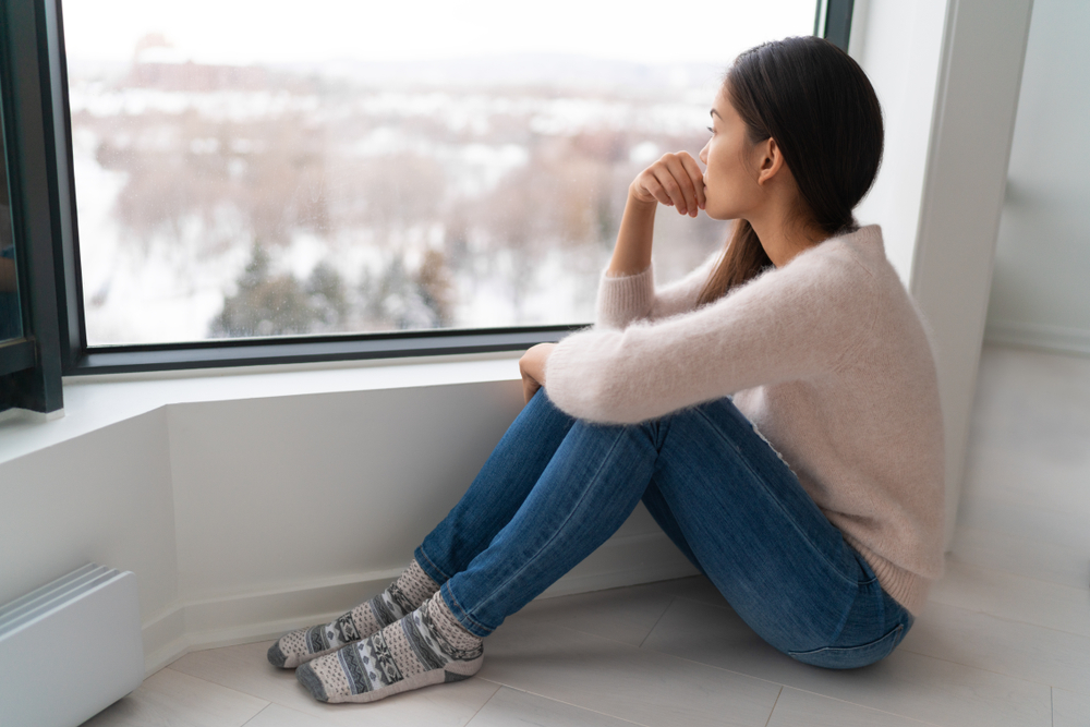Young woman looks out window sadly on snowy winter day