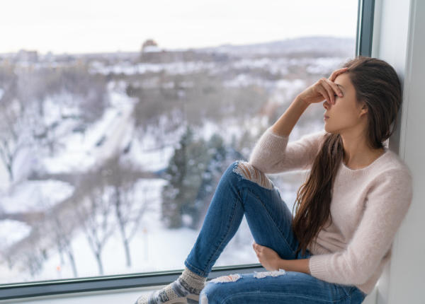 A person sitting on a window sill with their head in their hands
